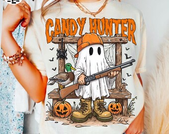 May include: Cream-colored t-shirt with the text "CANDY HUNTER" in orange. The graphic features a ghost character wearing an orange cap and holding a shotgun, with pumpkins, a duck, and a spider web design.