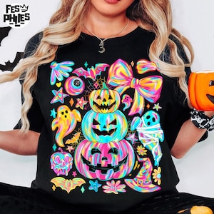 May include: Black t-shirt featuring a vibrant Halloween design. The graphic includes stacked jack-o'-lanterns, ghosts, bats, bows, and stars in neon rainbow colors. The shirt has a classic crew neck and short sleeves, perfect for the spooky season.