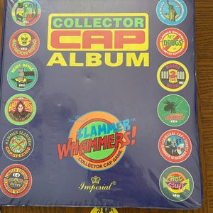 May include: A blue Collector Cap Album for Slammer Whammers, with colorful circular caps around the edges. The album has the words "Collector Cap Album" in yellow and red. The album is made by Imperial.