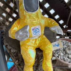 May include: A plush doll in a yellow hazmat suit with a black face shield and silver gloves. The doll has an "Intel Inside" logo on the chest and an "intel" tag.