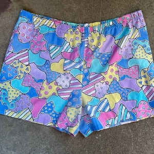 May include: A pair of colorful patterned shorts with a geometric design in shades of pink, blue, yellow, and purple.