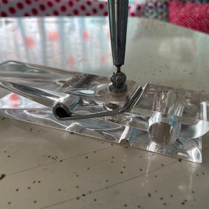 May include: A clear acrylic pen holder shaped like a clothespin with a metal spring and a silver pen.