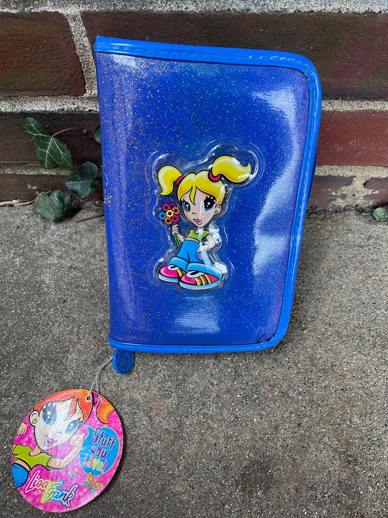 Puede incluir: Estuche azul brillante con un dise&ntilde;o de ni&ntilde;a de dibujos animados. El estuche tiene cierre de cremallera y ribete azul a juego. Una etiqueta de Lisa Frank est&aacute; adjunta.