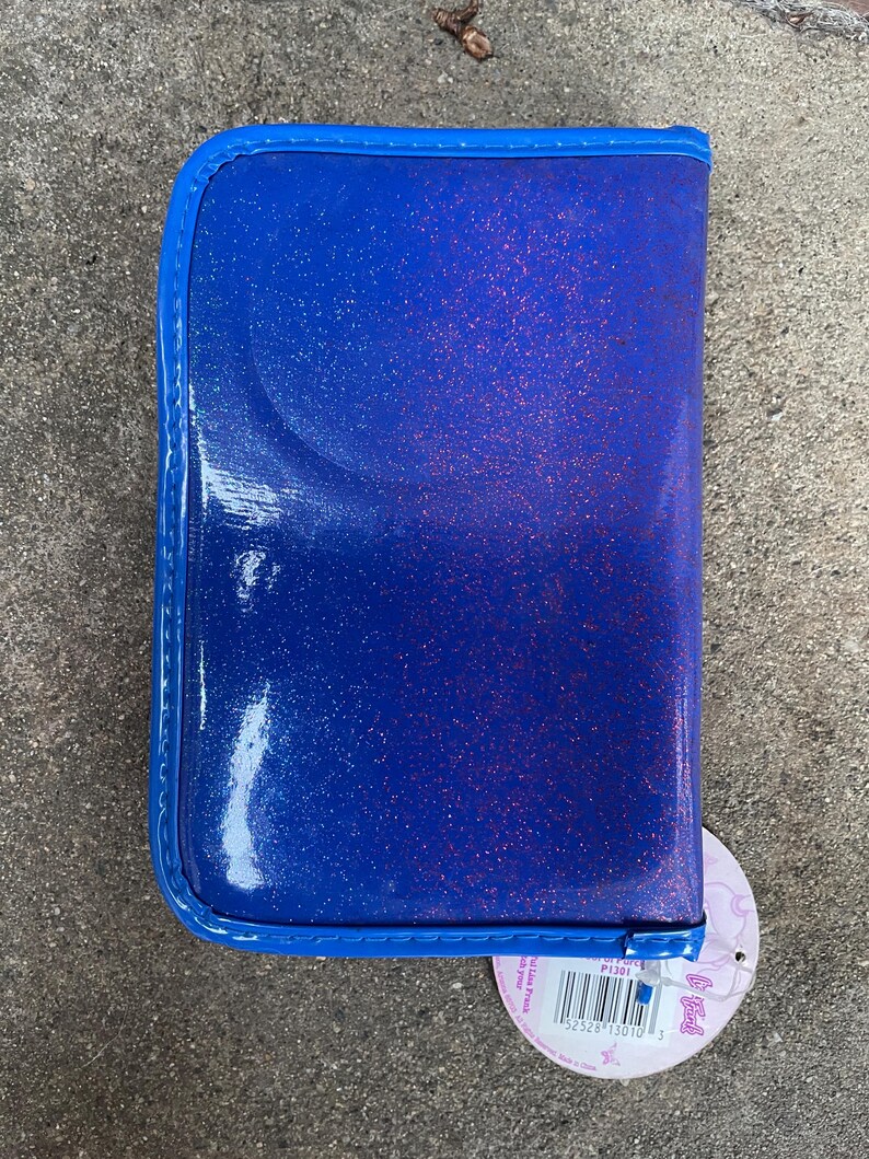 Puede incluir: Un estuche azul brillante con un borde azul a juego. El estuche tiene un acabado brillante y un cierre de cremallera. Una etiqueta redonda con un c&oacute;digo de barras est&aacute; adjunta en la esquina inferior derecha.