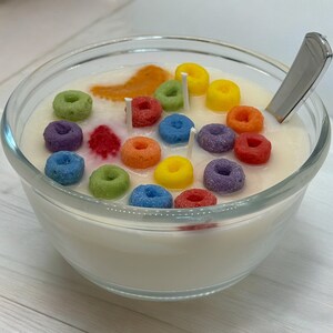 May include: A glass bowl filled with white wax and colorful cereal-shaped candles. The candles are arranged in a circular pattern and have a variety of colors, including red, orange, yellow, green, blue, and purple.