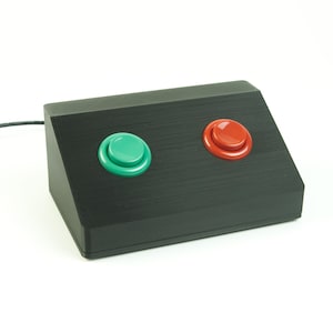 May include: A black box with two buttons, one green and one red. The box is connected to a black cable.
