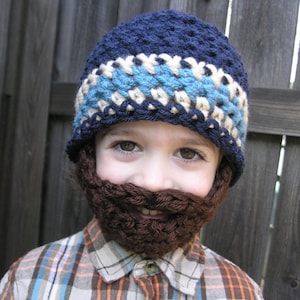 May include: A child wearing a blue and white crocheted hat with a brown crocheted beard attached. The child is wearing a plaid shirt.