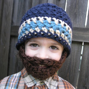 May include: A child wearing a blue, white and brown crocheted hat with a beard. The hat has a blue and white striped band.