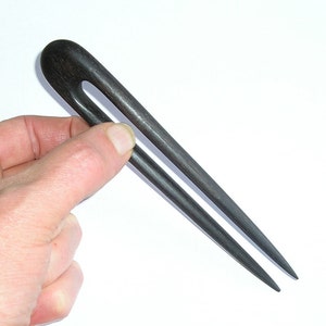 Op de afbeelding: Een zwarte houten haarstick met een eenvoudig ontwerp. De stick is ongeveer 25 cm lang en heeft een afgerond uiteinde.