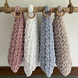 Può includere: Quattro panni da cucina in maglia appesi a un ramo di legno. I panni da cucina sono rosa, bianco, azzurro e beige.