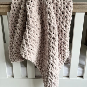 May include: A soft, light pink knitted baby blanket draped over a white crib.