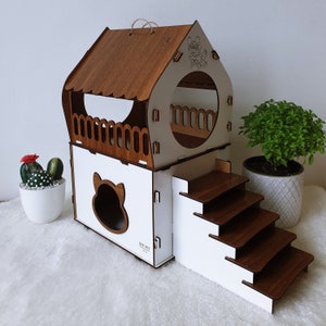 Puede incluir: Una casa para gatos de madera con una base blanca y un techo marrón. La casa tiene una pequeña abertura para que el gato pueda entrar y una plataforma con escalones que conducen a ella. La casa está decorada con una pequeña silueta de gato y las palabras "Love Pets".