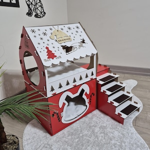 May include: A red and white wooden pet house with a Christmas theme. The house features a sloped roof with snowflake and Christmas tree cutouts, and a small tag that says "Brownie". The house has a bunny-shaped entrance and a set of stairs.