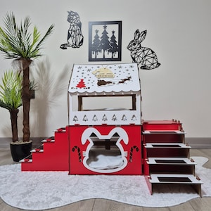 May include: A red and white wooden pet house with a multi-level design. The house features a bunny-shaped entrance, stairs, and a rooftop with a Christmas theme, including a sleigh and the word "Brownie". Decorative cat, tree, and rabbit wall art are visible.
