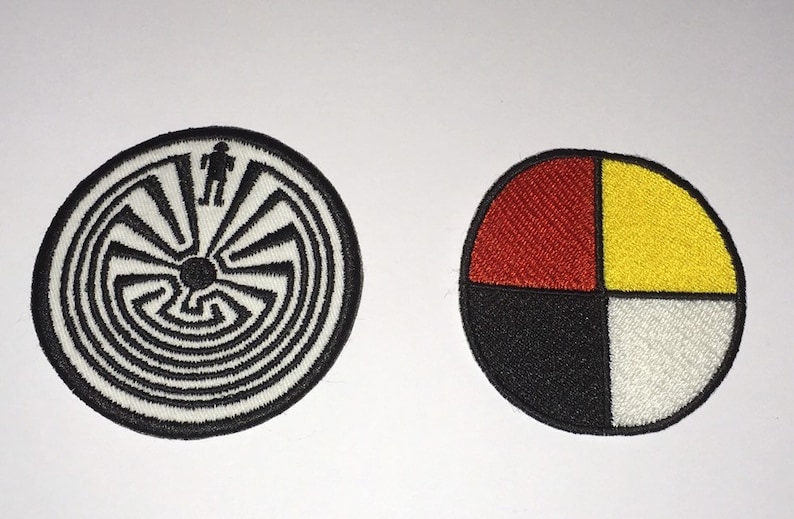 May include: Two embroidered patches. The first patch is white with a black and white spiral maze design. The second patch is a circle divided into four sections: red, yellow, black, and white.