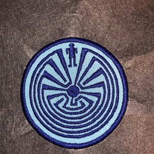 May include: A blue and navy blue embroidered patch featuring a Native American symbol, a circular maze with a figure standing in the center.