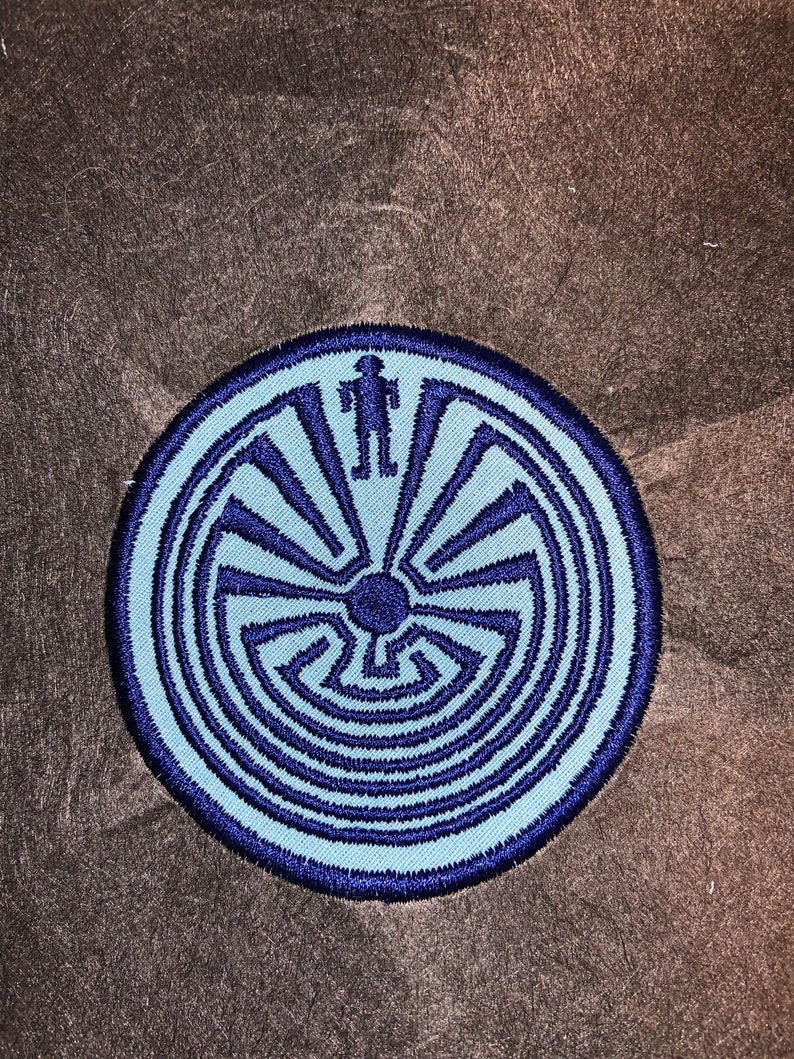 May include: A blue and navy blue embroidered patch featuring a Native American symbol, a circular maze with a figure standing in the center.