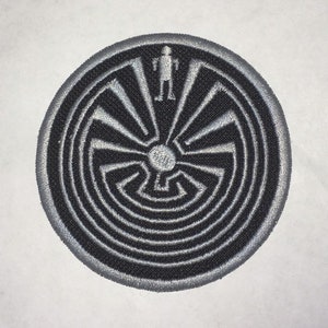 May include: A black and silver embroidered patch featuring a Native American symbol, a circular maze with a figure standing in the center.