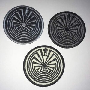 May include: Three embroidered patches featuring a black and white labyrinth design with a stylized human figure at the top. The patches are circular and have a gray, black, and white background.