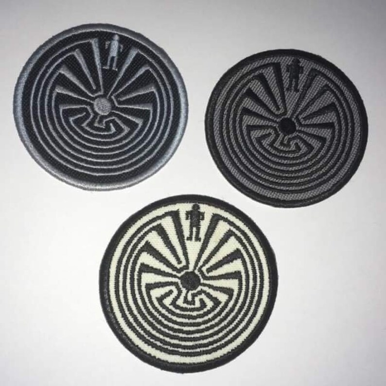 May include: Three embroidered patches featuring a black and white labyrinth design with a stylized human figure at the top. The patches are circular and have a gray, black, and white background.