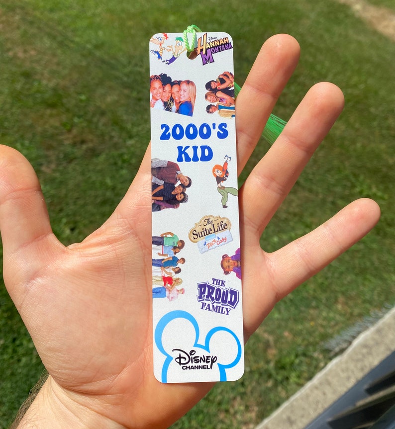 Puede incluir: Un marcap&aacute;ginas blanco con el logotipo de Disney Channel y el texto "2000's Kid". El marcap&aacute;ginas presenta im&aacute;genes de programas populares de Disney Channel de la d&eacute;cada de 2000, como "Hannah Montana", "Zack y Cody: Gemelos en acci&oacute;n" y "Los Proud".