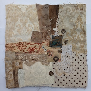 Könnte beinhalten: Eine quadratische Stoffcollage aus verschiedenen Textilresten in Beige-, Braun- und Cremetönen. Das Stück enthält Damastmuster, Punkte, Spitzenbesatz und einen kleinen quadratischen Flicken mit einer Vogelillustration, akzentuiert durch verschiedene Knöpfe.