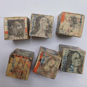 May include: Six vintage wooden blocks, each featuring a different image of a woman's face and map fragments. The blocks are covered in aged paper with faded colours, including orange, blue, and beige. The blocks are arranged on a white surface.