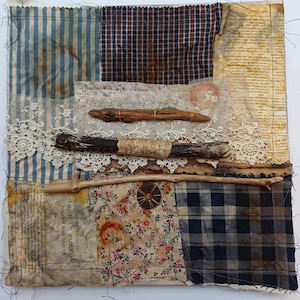 May include: A patchwork textile artwork featuring diverse fabrics: blue-striped, floral, and plaid. Driftwood and lace are layered across the surface, with a button detail. The piece has a rustic, handmade aesthetic, with a variety of textures and patterns.