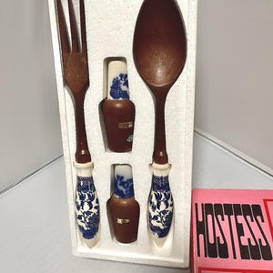 May include: A vintage serving set featuring a fork and spoon with brown wooden utensils and white handles with blue floral designs. The set includes two small brown bottles with blue and white designs. The set is in a white foam insert.