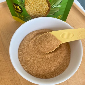 以下が含まれることがあります： 白いボウルに、黄金色の茶色の砂糖の代用品が入っています。黄色いスプーンが乗っています。砂糖の代用品のパッケージには、「0%カロリー」と「ゴールデン」と書いてあります。