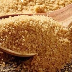 May include: A close-up of brown granulated sugar in a wooden spoon. The sugar is a light brown color and has a grainy texture.