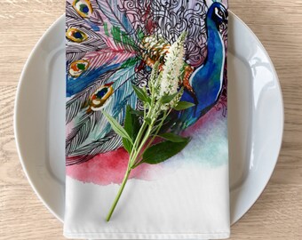 May include: A white linen napkin with a colorful watercolor design of a peacock with a white flower sprig on top. The peacock has blue and green feathers and a black and white patterned design.