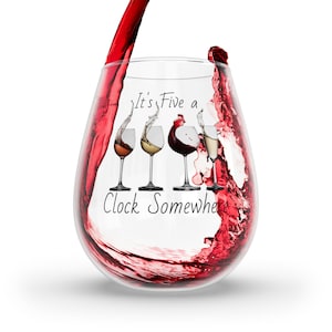 May include: A clear glass wine glass with a red wine pour. The glass has the text "It's Five o'Clock Somewhere" printed on it.