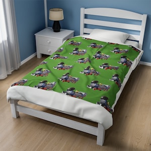 May include: A green twin-sized bedspread with a repeating pattern of a blue and red toy train. The bedspread is on a white bed frame with a white nightstand next to it.