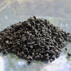 May include: A pile of dark gray, irregularly shaped, porous rocks. The rocks have a rough texture and vary in size, creating a textured appearance. The image is taken in natural light, highlighting the details of the rocks.