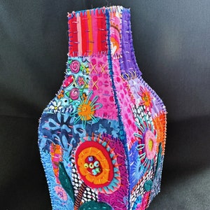 May include: A colorful patchwork fabric vase with a geometric design. The vase is made of different fabrics sewn together in a patchwork style. The vase is decorated with flowers and other designs. The vase is a unique and handmade piece of art.