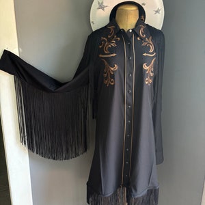 Op de afbeelding: Een zwart lang mouw shirt met franjes aan de mouwen en zoom. Het shirt heeft een western-stijl kraag en gouden borduurwerk aan de voorkant.