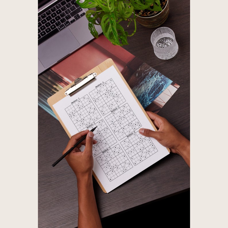 Puede incluir: Una persona est&aacute; trabajando en un conjunto de seis rompecabezas de Sudoku en un portapapeles. Los rompecabezas est&aacute;n etiquetados como "Medio 1" a "Medio 6".