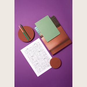 Puede incluir: Una superficie morada con dos l&aacute;pices verdes, una libreta con estampado marr&oacute;n y blanco, una libreta verde, un c&iacute;rculo marr&oacute;n y una hoja de papel con seis rompecabezas de Sudoku. Los rompecabezas est&aacute;n etiquetados como "Cuadr&iacute;cula 1", "Cuadr&iacute;cula 2", "Cuadr&iacute;cula 3", "Cuadr&iacute;cula 4", "Cuadr&iacute;cula 5" y "Cuadr&iacute;cula 6".