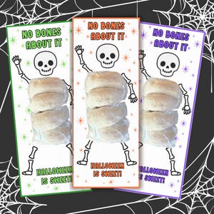 May include: Three rectangular cards featuring a black line drawing of a skeleton, the text NO BONES ABOUT IT and HALLOWEEN IS SWEET, and a clear plastic bag containing four round baked goods attached to the center of each card in green, orange, and purple.