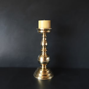 May include: A gold metal candle holder with a round base and a single candle on top.