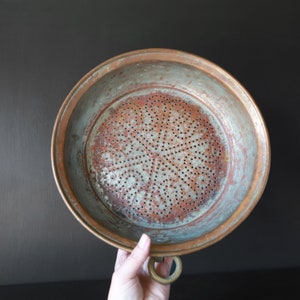 May include: A copper strainer with a decorative pattern of holes. The strainer has a handle with a ring at the end.