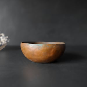 May include: A copper bowl with a hammered finish. The bowl has a slightly irregular shape and a warm, aged patina.