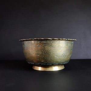 May include: A large, round, brass bowl with a scalloped rim and intricate etched designs. The bowl has a green patina and is decorated with floral and geometric patterns.