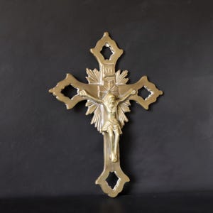 May include: A gold-colored crucifix with a detailed depiction of Jesus Christ. The cross features ornate cut-out designs and a sunburst pattern behind the figure. The figure of Christ is in a traditional pose.