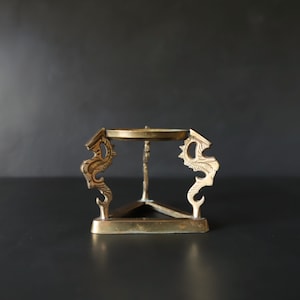 May include: A gold metal decorative stand with a round top and three legs. Each leg is shaped like a stylized dragon with intricate details.