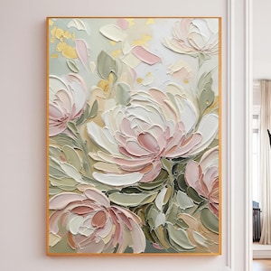 May include: A framed floral painting with a gold border. The artwork features large, textured flowers in shades of white, pink, and cream, with green leaves and gold accents. The painting is displayed on a white wall.