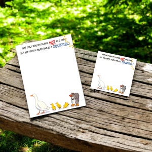 Könnte beinhalten: Zwei weiße Notizblöcke mit einer Cartoon-Ente, Entenküken und einem Eichhörnchen. Der Text auf den Notizblöcken lautet: „NOT ONLY ARE MY DUCKS NOT IN A ROW, BUT I'M PRETTY SURE ONE IS A SQUIRREL!“ Die Notizblöcke liegen auf einer Holzoberfläche.