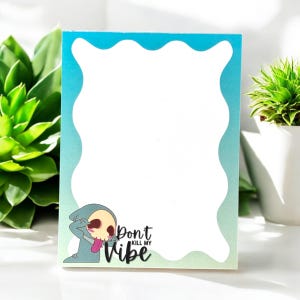 May include: A rectangular notepad with a blue and white wavy border. The notepad features a cartoon illustration of a skull with a tongue sticking out and the text "Don't Kill My Vibe".
