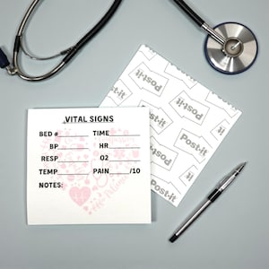 Könnte beinhalten: Ein medizinisches Stillleben mit einem Stethoskop, einem Stift und einem Notizblock mit den Worten "VITAL SIGNS" und Feldern zur Aufzeichnung von Patientendaten. Ein Post-it ist ebenfalls sichtbar. Der Notizblock hat ein rosa Herz und ein Blumenmuster.